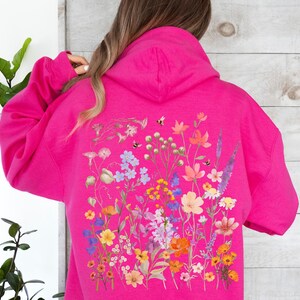 May include: A pink hoodie with a floral print on the back. The print features a variety of flowers in shades of pink, purple, yellow, and orange.