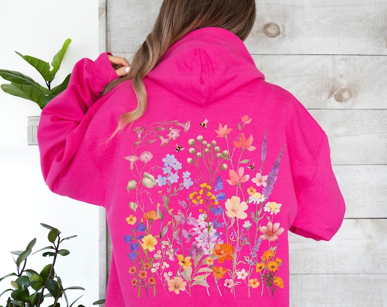 May include: A pink hoodie with a floral print on the back. The print features a variety of flowers in shades of pink, purple, yellow, and orange.