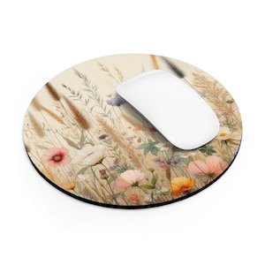 May include: A round mouse mat with a floral design featuring a variety of wildflowers and grasses in shades of pink, yellow, white, and brown on a beige background.