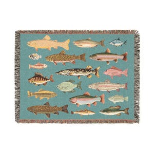 May include: A woven throw blanket featuring a teal background with various fish illustrations in shades of tan, brown, pink, and green. The blanket has a fringed border in a complementary color, adding a decorative touch to the design.