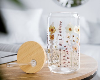 Puede incluir: Una botella de agua reutilizable de vidrio transparente con tapa de bambú y una pajita. La botella tiene un diseño floral con flores y hojas prensadas.