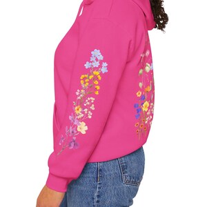 May include: A pink hoodie with a floral design on the sleeve. The flowers are in shades of blue, yellow, and purple.