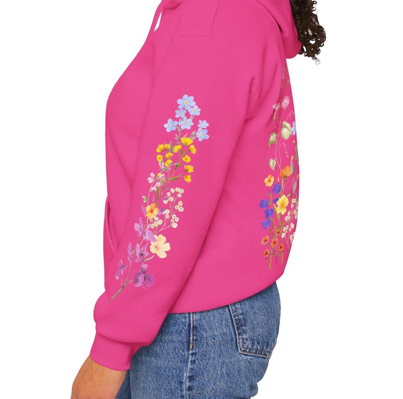 May include: A pink hoodie with a floral design on the sleeve. The flowers are in shades of blue, yellow, and purple.