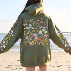 May include: A green hooded sweatshirt with a floral print on the front and sleeves. The flowers are in shades of pink, purple, yellow, and white.