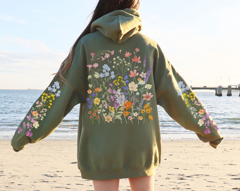 May include: A green hooded sweatshirt with a floral print on the front and sleeves. The flowers are in shades of pink, purple, yellow, and white.