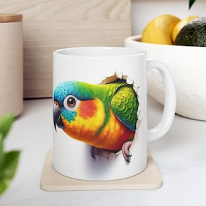 Könnte beinhalten: Eine weiße Keramiktasse mit einem bunten Papagei, der aus einem Loch in der Seite schaut. Der Papagei hat blaue, grüne, gelbe und orangefarbene Federn.