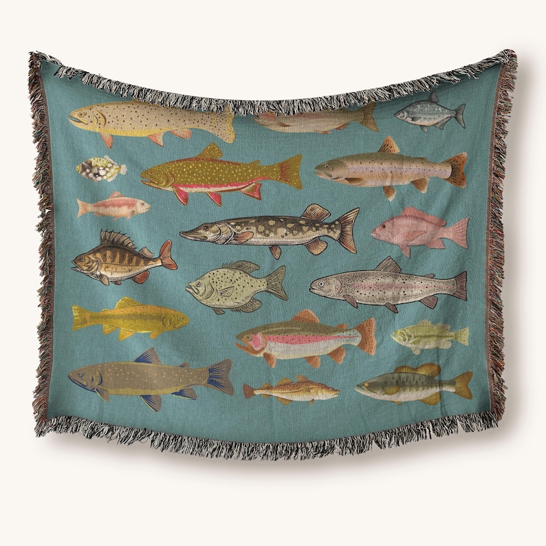 May include: A teal throw blanket featuring a variety of illustrated fish in shades of yellow, red, and brown. The blanket has a fringed edge and is suitable for a bed or sofa. The fish are arranged in a repeating pattern.