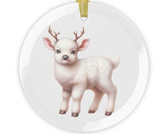May include: A white ceramic Christmas ornament featuring a charming illustration of a baby deer with small antlers and white spots. The deer has pink ears and brown hooves. A gold ribbon is attached for hanging.