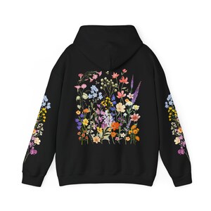 May include: Black hooded sweatshirt with a floral print on the back and sleeves. The print features a variety of colorful flowers and leaves.