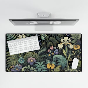 Puede incluir: Alfombrilla de escritorio rectangular con un diseño floral con iris, pensamientos y otras flores en tonos amarillos, morados y verdes sobre un fondo negro. Un teclado y un ratón blancos están sobre la alfombrilla. Un monitor de ordenador está encima.