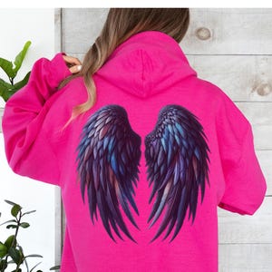 May include: A bright pink hoodie with a large graphic of black angel wings on the back. The wings have iridescent blue and purple accents.