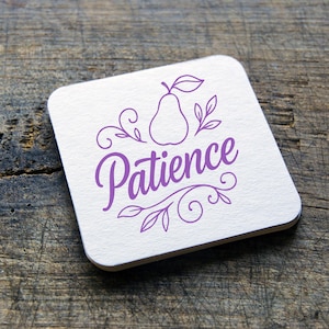 May include: Square white coaster with the word "Patience" in a purple script font, along with a pear illustration and decorative leaves. The coaster is on a wooden surface.