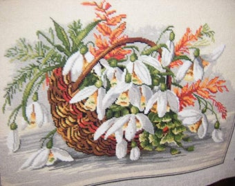 Op de afbeelding: Een witte rieten mand vol witte sneeuwklokjes en oranje en rood blad.
