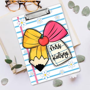 May include: A clipboard with a whimsical design featuring a yellow pencil, a pink bow, and a red apple. The clipboard has blue and white stripes, daisies, and the name "Mrs. Kelsey" on a notepad. A pair of eyeglasses rests on a book.