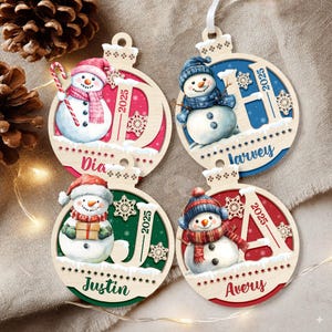 May include: Four circular wooden Christmas ornaments featuring illustrations of snowmen. Each ornament displays a large letter, the year 2025, and a personalized name: Dia, Harvey, Justin, and Avery. The designs include snowflakes and candy canes.