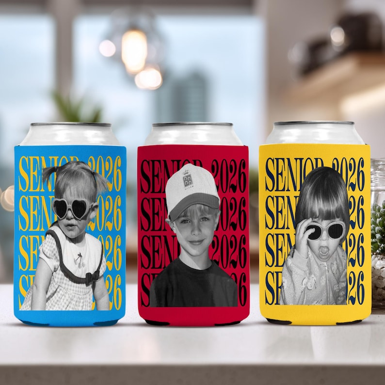 Puede incluir: Tres enfriadores de latas con fotos de ni&ntilde;os. Los enfriadores son azules, rojos y amarillos. Cada enfriador tiene la inscripci&oacute;n "SENIOR 2026" en un patr&oacute;n repetido. Las fotos son en blanco y negro.