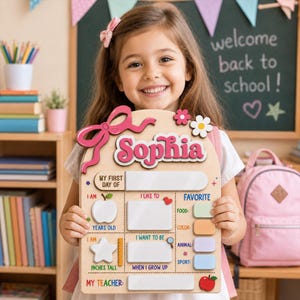 May include: A wooden first day of school sign featuring the name Sophia in pink letters, a large pink bow, and white blank spaces for writing details like age, height, favorite food, color, animal, sport, and teacher, decorated with colorful icons.