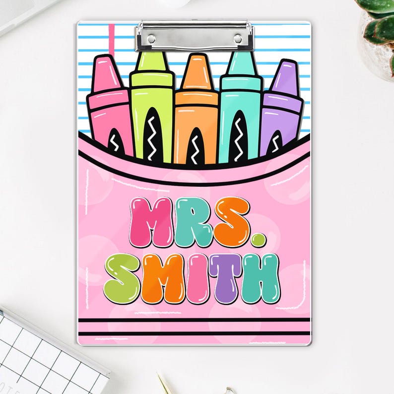 May include: A pink clipboard with a colorful crayon design. The design includes pink, green, orange, blue, and purple crayons in a pink pouch. The text "MRS. SMITH" is displayed in bubble letters.
