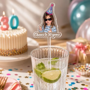 Puede incluir: Un agitador de bebidas de acr&iacute;lico transparente con un recorte de una persona con gafas de sol y un gorro de fiesta rosa y azul con el n&uacute;mero 30, con el texto Cheers to 30 years impreso en blanco en la base del dise&ntilde;o.