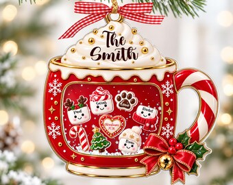 May include: A red Christmas ornament shaped like a mug filled with whipped cream, topped with a red and white gingham ribbon. The mug features the text The Smith, candy cane handle, and illustrations of marshmallows, a tree, and a heart.