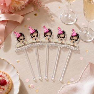 Puede incluir: Cinco agitadores de bebidas de acr&iacute;lico transparente con la imagen impresa de una persona con un sombrero de fiesta rosa con estampado de corazones y gafas de sol negras, sosteniendo un micr&oacute;fono. El texto Cheers to 30 years est&aacute; en blanco.