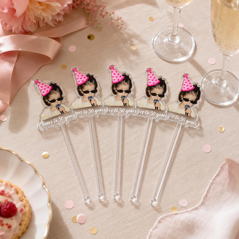 Puede incluir: Cinco agitadores de bebidas de acr&iacute;lico transparente con la imagen impresa de una persona con un sombrero de fiesta rosa con estampado de corazones y gafas de sol negras, sosteniendo un micr&oacute;fono. El texto Cheers to 30 years est&aacute; en blanco.