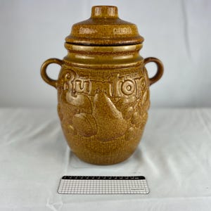 May include: A brown ceramic jar with a lid, decorated with a raised design of fruit and the word "BUTTER" in a stylised font.