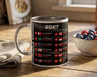 May include: A black ceramic mug featuring the text 2027 Formula Racing and a list of race dates, locations, and national flags. The mug has a silver-toned handle and interior, displaying a schedule of international racing events in a vertical layout.