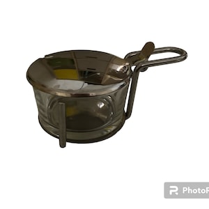 Peut inclure: Un pot à sel en argent et en verre avec un couvercle à charnière et une poignée. Le pot à sel est sur un fond blanc.