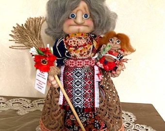 May include: A handmade doll depicting a woman in traditional Ukrainian attire. The doll has gray hair, blue eyes, and holds a broom and a smaller doll. The woman's outfit includes a patterned skirt and a detailed bodice.
