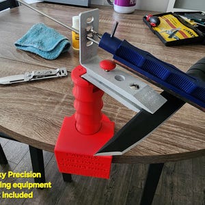 May include: A knife sharpening system with a red base, silver guide, and blue handle. A silver folding knife and a blue cloth are also visible. The text "Lansky Precision Sharpening equipment not included" is at the bottom.