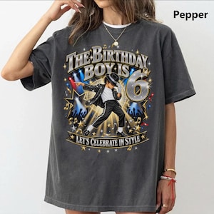 May include: A charcoal gray t-shirt featuring a graphic of a person in a sequined jacket and fedora dancing. The text reads The Birthday Boy Is 6 and Let's Celebrate In Style. The design includes gold stars, musical notes, and spotlights.