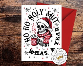 May include: A white greeting card featuring a black and red illustration of a skeleton wearing a Santa hat and a patterned scarf, holding a mug of hot cocoa with marshmallows. The text reads HO HO HOLY SHIT WHAT A YEAR, surrounded by snowflakes.
