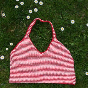 Könnte beinhalten: Ein rot-weiß gestreiftes Häkeltop mit Halter. Das Top hat einen V-Ausschnitt und einen Halteriemen. Es liegt auf grünem Gras, auf dem kleine weiße Gänseblümchen verstreut sind.