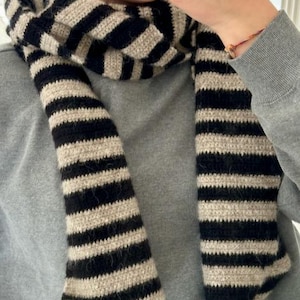 Könnte beinhalten: Ein gestrickter Schal in Schwarz und Beige mit Streifen. Der Schal ist aus weichem, flauschigem Garn.