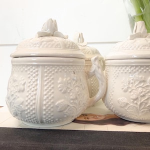 May include: A set of three ceramic mugs with a speckled, matte finish. The mugs are in shades of cream, light gray, and dark gray. Each mug has a simple, minimalist design and a rounded handle.