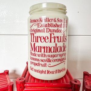 May include: A vintage jar of Three Fruits Marmalade, with red lettering on a cream-colored glass jar. The text includes "James Keiller & Son Ltd, Established 1797, Original Dundee." The jar is 16 oz (1 lb) and sits on a red bamboo stand.