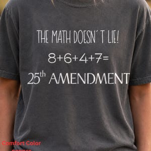 May include: Dark grey t-shirt with white text that reads "THE MATH DOESN'T LIE! 8+6+4+7= 25th AMENDMENT". The shirt is a Comfort Color brand in the color pepper. The shirt has short sleeves and a crew neck.