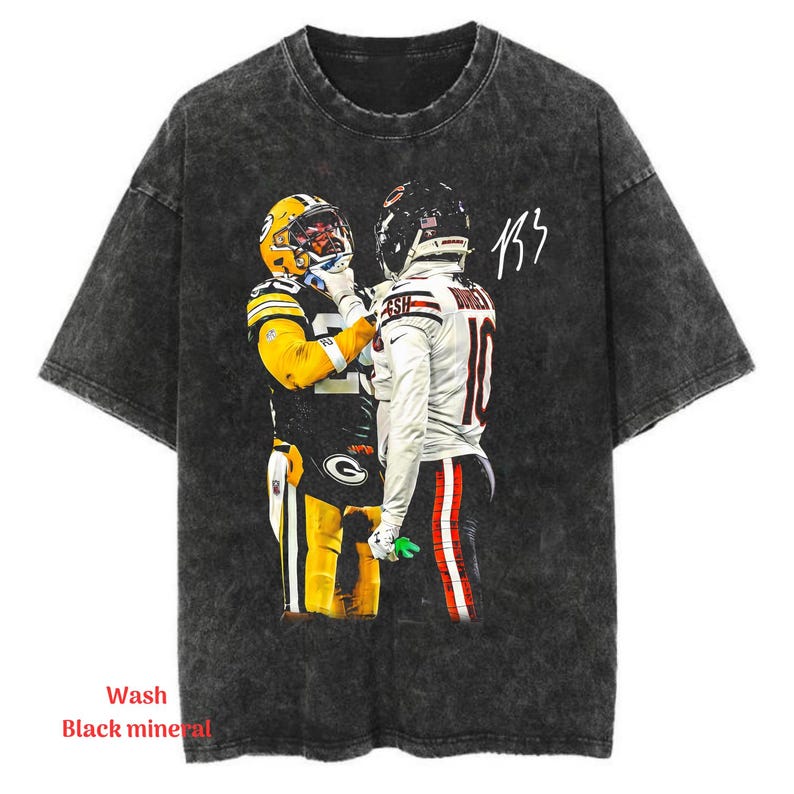 May include: A black mineral wash short-sleeve t-shirt featuring a graphic print of two football players in team uniforms facing each other. One player wears a yellow and green jersey, while the other wears a white jersey with the number 10.