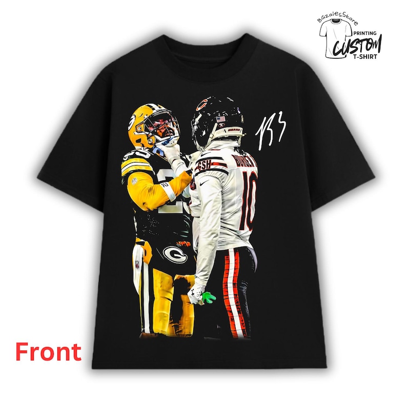 May include: A black short-sleeve t-shirt featuring a graphic print of two American football players in opposing uniforms facing each other. One player wears a yellow and green jersey, while the other wears a white jersey. Includes a handwritten signature.