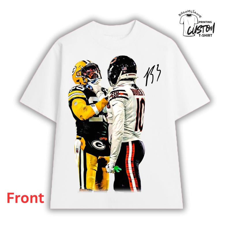 May include: A white short-sleeve t-shirt featuring a graphic print of two American football players in opposing uniforms facing each other. One player wears a yellow and green uniform, the other a white and navy uniform. Includes a black signature.