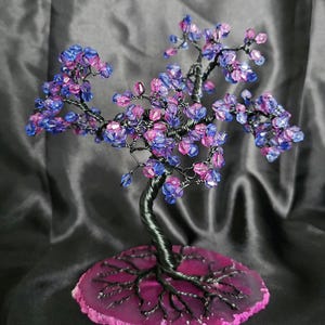 Könnte beinhalten: Eine Drahtskulptur eines Baumes mit einer rosa Achatbasis. Der Baum ist mit blauen und rosa Glasperlen verziert.