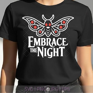 May include: Black t-shirt featuring a white and red moth design above the words "Embrace the Night" in white. The moth has red accents on its wings and head. The shirt is a classic crew neck style.