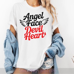 以下が含まれることがあります： 黒と赤で「Angel Face Devil Heart」の文字がプリントされた白いTシャツ。言葉は縦に配置され、「Face」の上に天使の羽があります。デニムジャケットが肩にかけられています。
