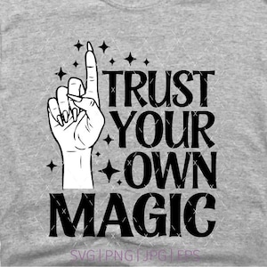 Puede incluir: Una camiseta gris jaspeado con un estampado gráfico negro de una mano con uñas largas apuntando hacia arriba, rodeada de pequeñas estrellas de cuatro puntas. El texto TRUST YOUR OWN MAGIC aparece en una fuente negra, negrita y serif.