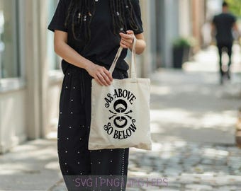 May include: A beige canvas tote bag featuring a black graphic print of two mirrored trees and the text "AS ABOVE SO BELOW" arranged in a circular pattern. The bag has two shoulder straps and a rectangular shape made of woven fabric material.