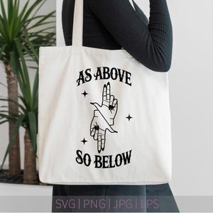 Könnte beinhalten: Cremefarbene Tragetasche mit dem Text "AS ABOVE SO BELOW" in schwarzer, gotischer Schrift. Die Tasche zeigt eine schwarze Grafik von zwei Händen in einer Geste, mit Sternen. Die Tasche wird von einer Person gehalten.