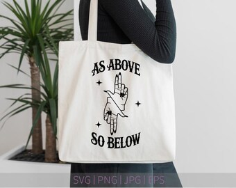 May include: Cream-colored tote bag with the text "AS ABOVE SO BELOW" in a black, gothic-style font. The bag features a black graphic of two hands in a gesture, with stars. The bag is held by a person.