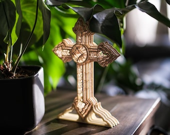 May include: A detailed, intricately carved wooden cross with a light brown finish. The cross is standing on a wooden table with green plants in the background.