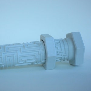 May include: A light gray, 3D-printed bolt with a geometric pattern on the cylindrical body. The bolt has a hexagonal head and a square nut-like feature. The object is set against a light blue background.